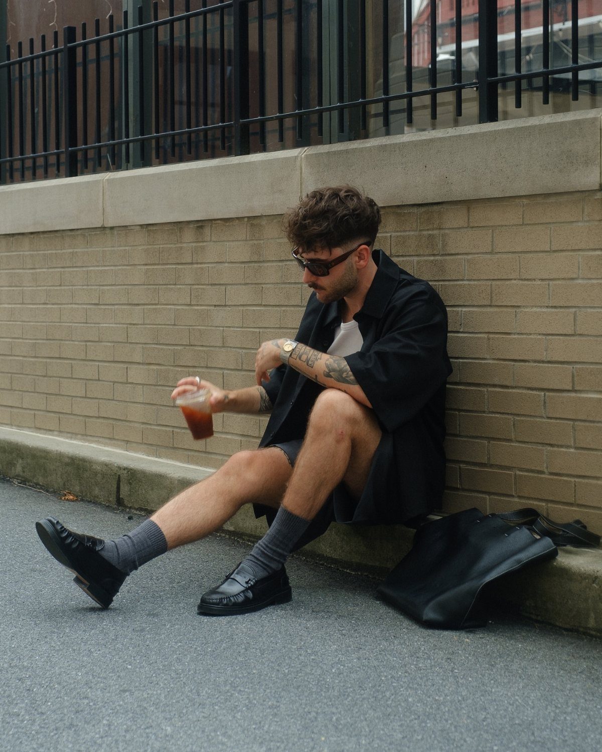 Man sitting on pavement wearing a black shirt and grey shorts outfit.