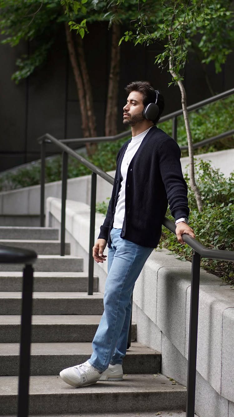 Man in black cardigan, white t-shirt, and light blue jeans on outdoor stairs.