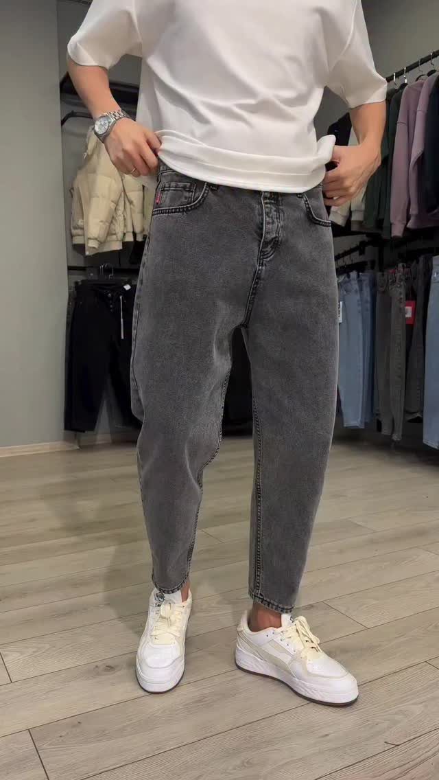 Man wearing grey denim jeans, a white t-shirt, and white sneakers in store.