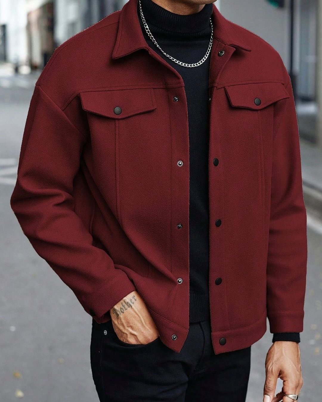 Man wearing a burgundy lightweight jacket over a black turtleneck and black trousers.