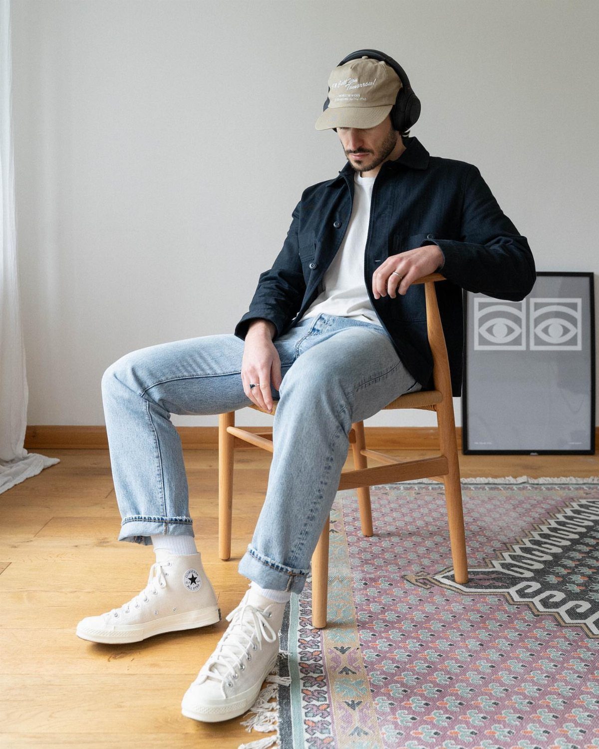 Man in casual attire wearing white high-top sneakers while sitting on a chair.