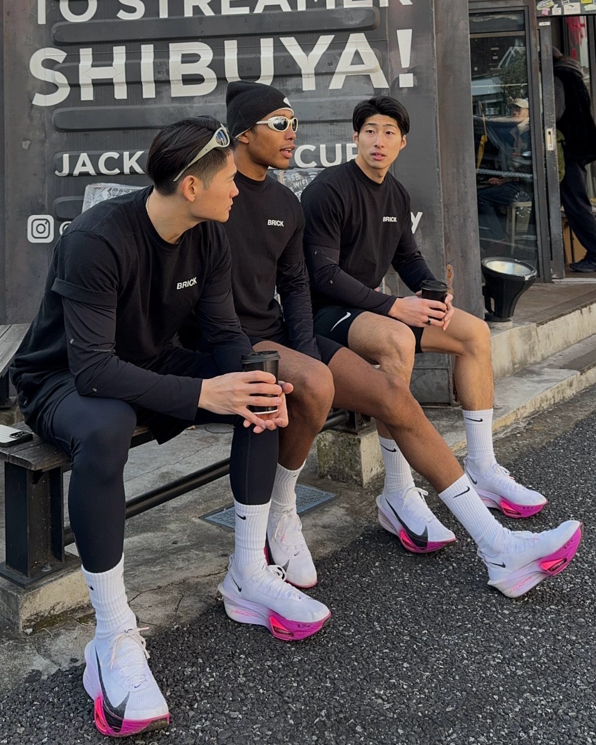 Three men in black athletic wear and white sneakers sitting on a bench.