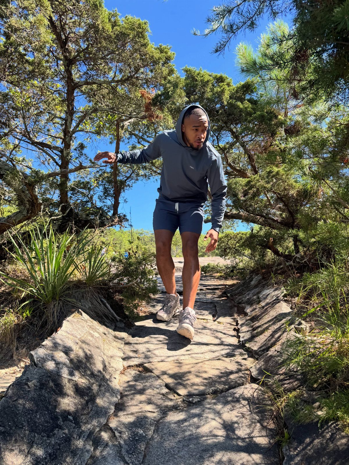 Man in grey hoodie and blue athletic shorts walking on rocky mountain path