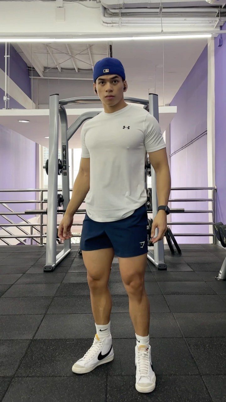 Muscular man in white short-sleeve workout shirt and blue shorts posing in gym
