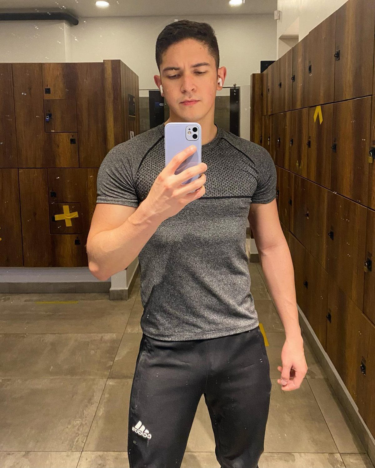 Man in grey athletic shirt taking a mirror selfie in gym locker room
