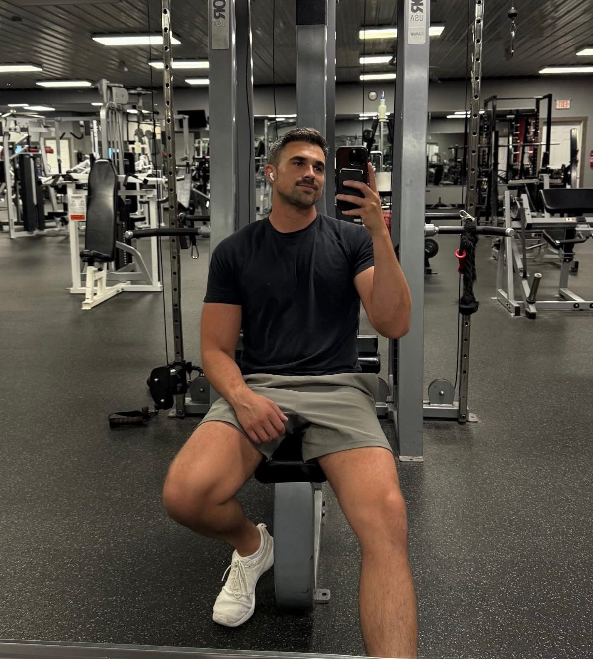 Muscular man taking a mirror selfie while sitting on a gym weight bench