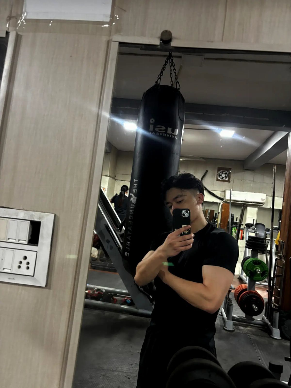 Muscular man in black t-shirt posing for a mirror selfie in a gym