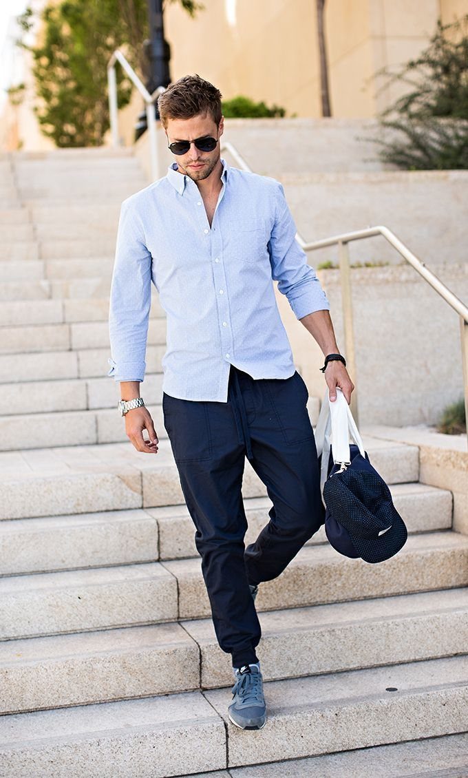 Man wearing a light blue button-up shirt and navy joggers walking down stairs.