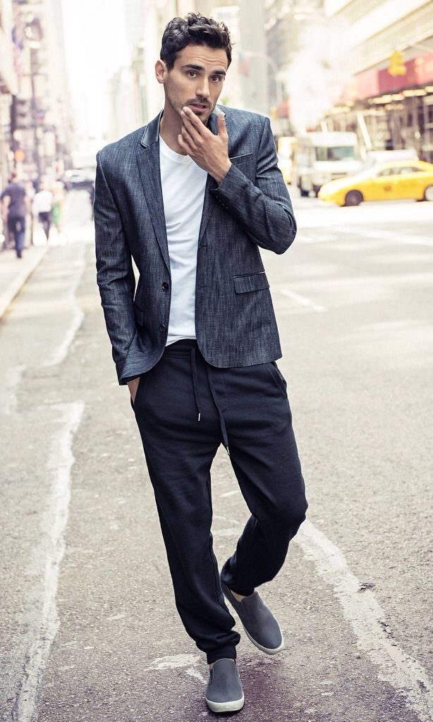 Man wearing a grey blazer and navy joggers standing on a city street.