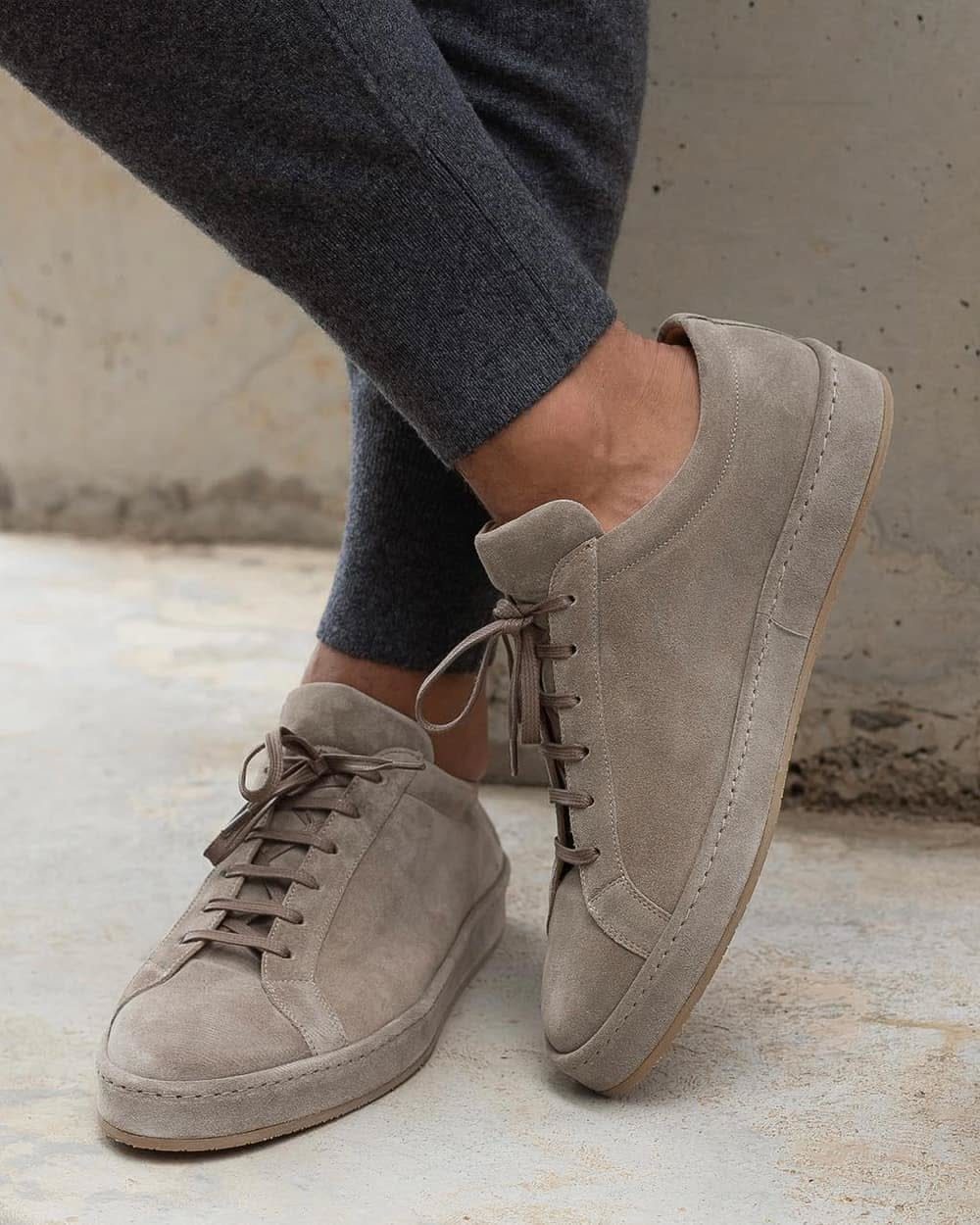 Beige suede sneakers paired with dark grey tapered joggers on a concrete floor.