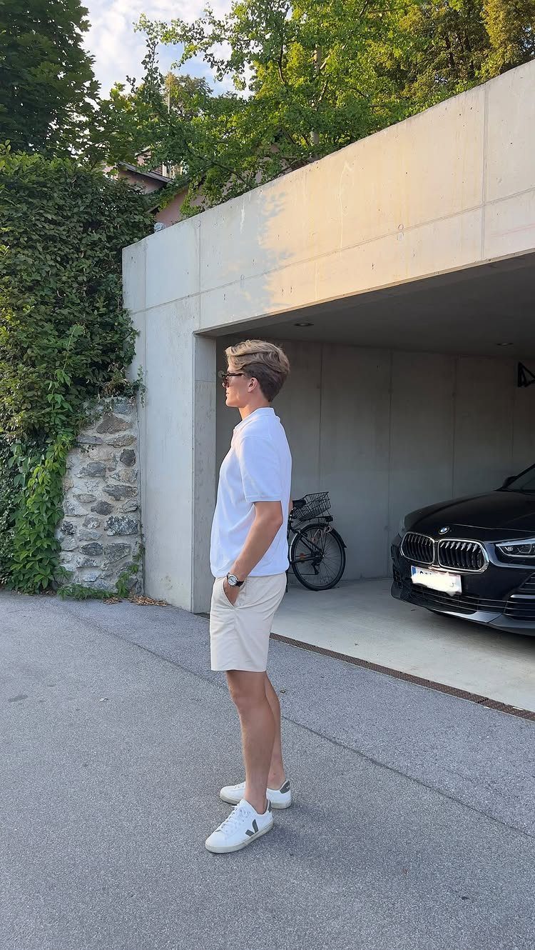 Man wearing a white t-shirt and off-white shorts standing by a concrete garage.