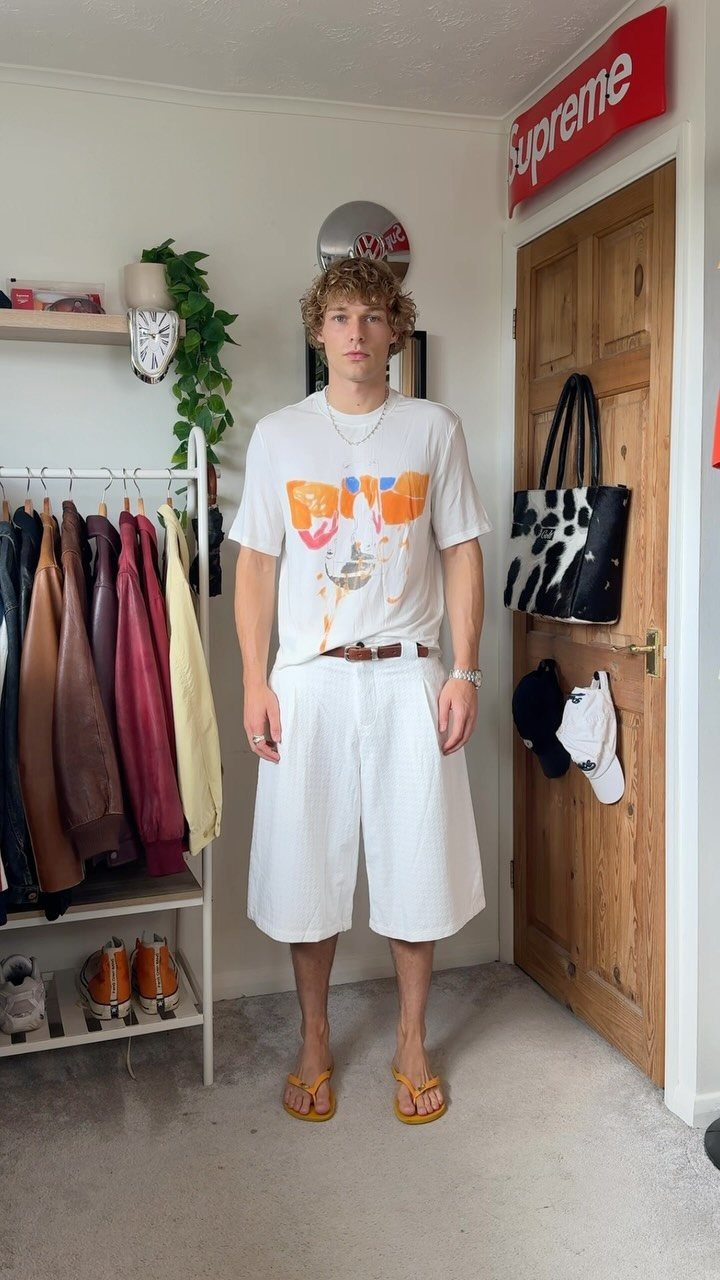Man wearing a white graphic t-shirt and wide-leg white shorts with yellow flip-flops.