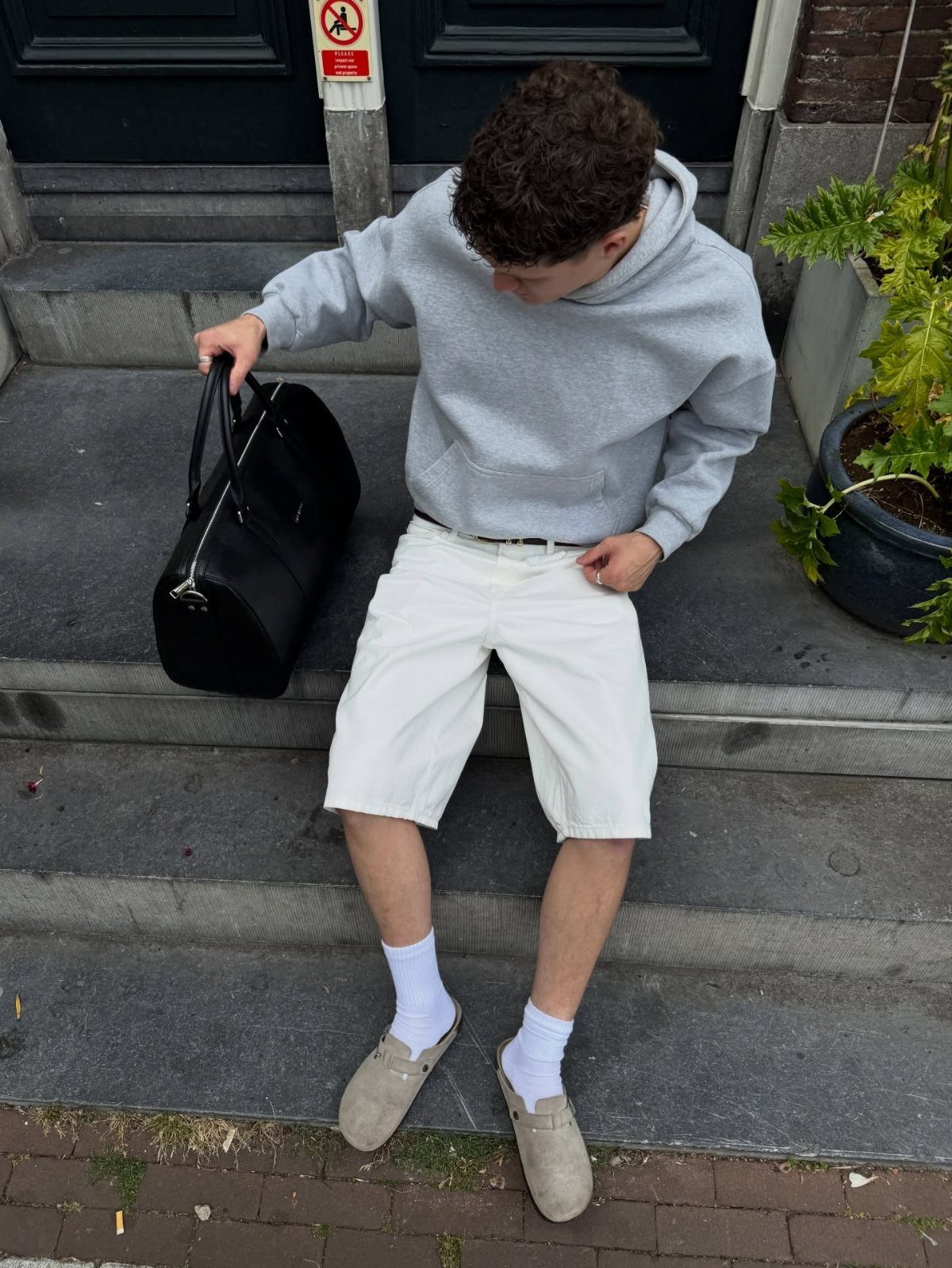 Man wearing a grey hoodie and white shorts with beige loafers on steps