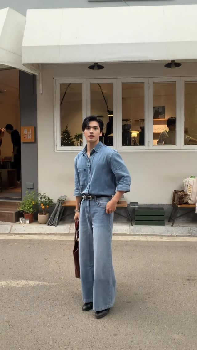 Man wearing a blue denim shirt and wide-leg blue jeans standing outdoors.