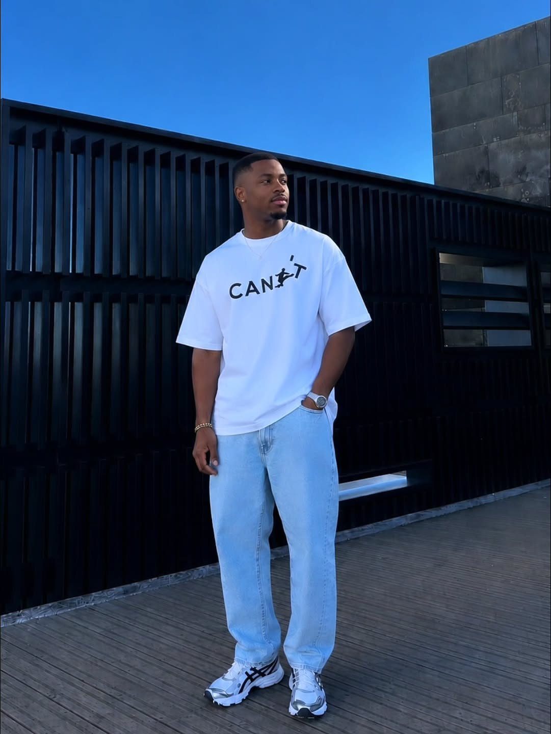 Man wearing a white graphic t-shirt, light blue jeans, and white sneakers.
