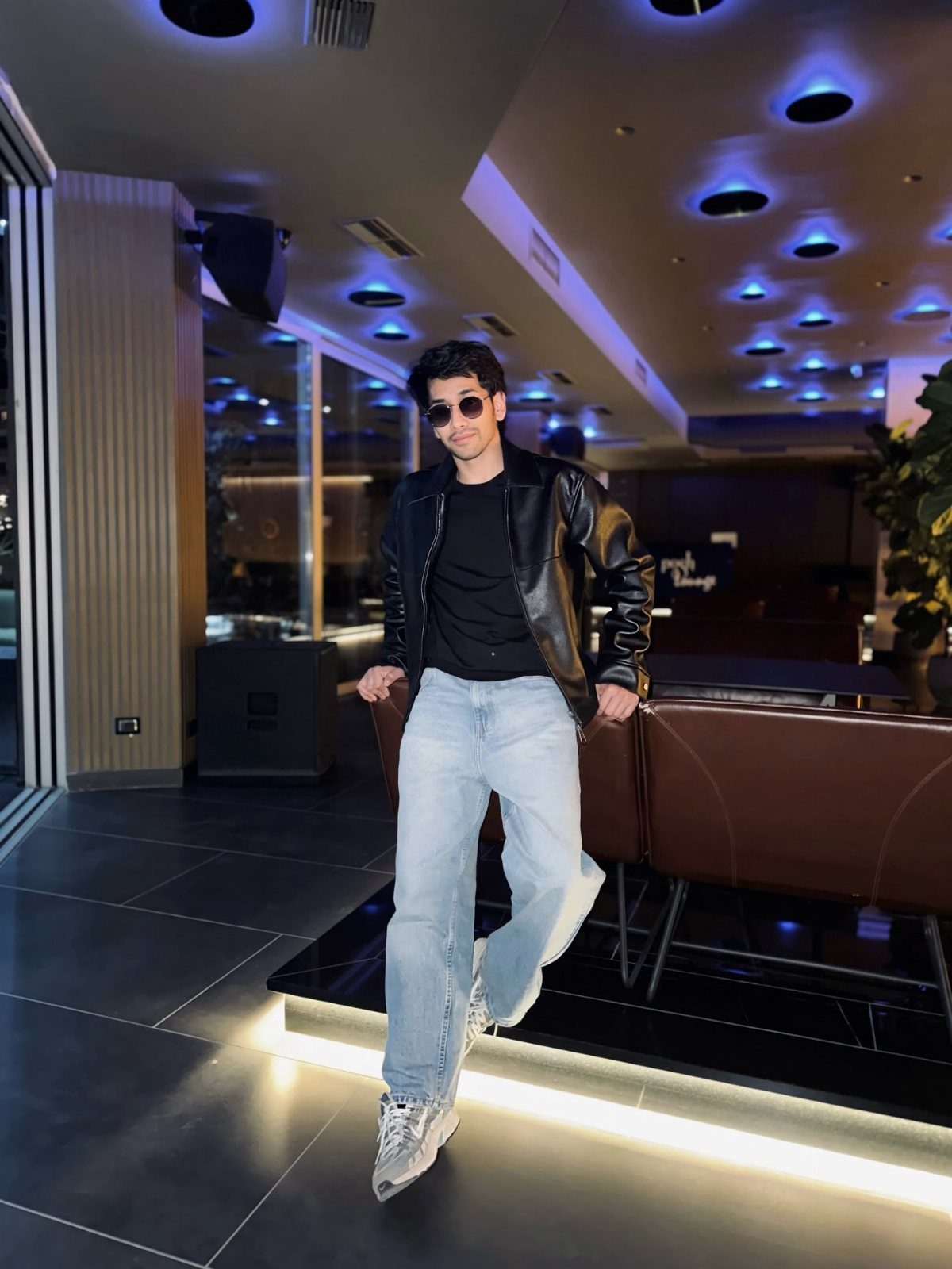 Man in black leather jacket, black t-shirt, and light blue wide-leg jeans.