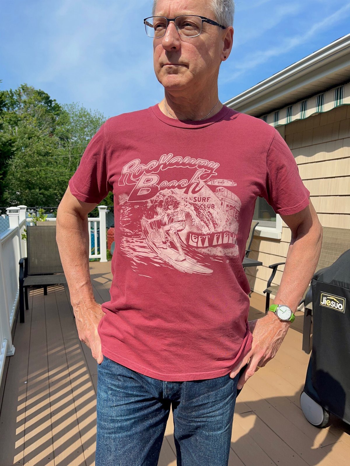 Middle-aged man wearing a red t-shirt and blue jeans on a wooden deck.