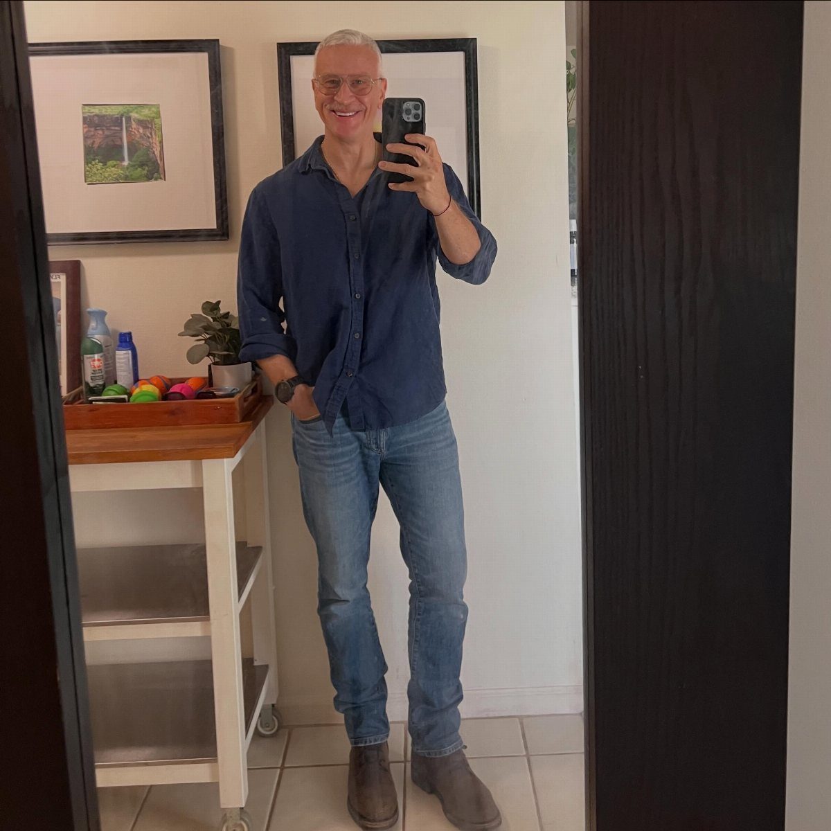 Older man wearing a blue shirt and slim fit blue jeans taking a selfie.