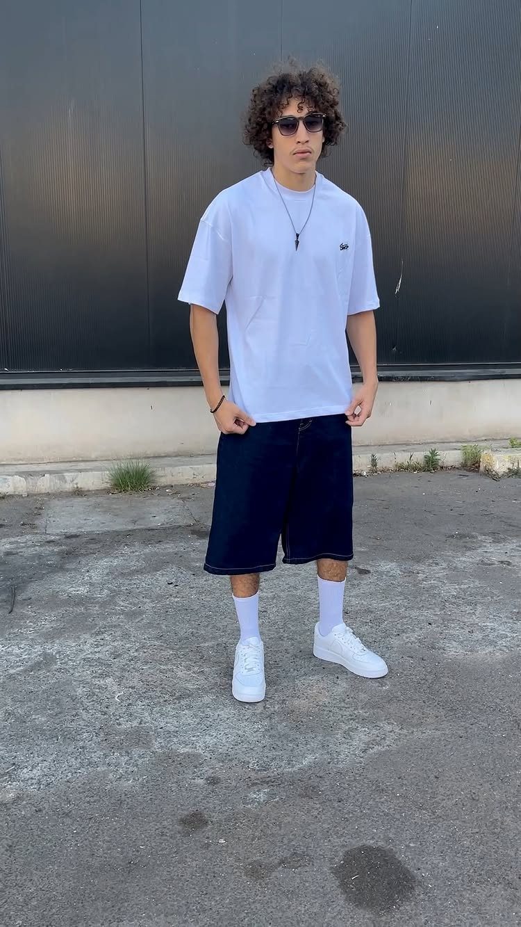 Man wearing a white t-shirt and baggy dark blue denim shorts with sneakers