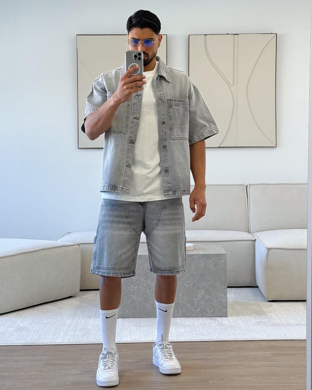 Man wearing a grey button-down denim shirt and matching denim shorts with white sneakers.