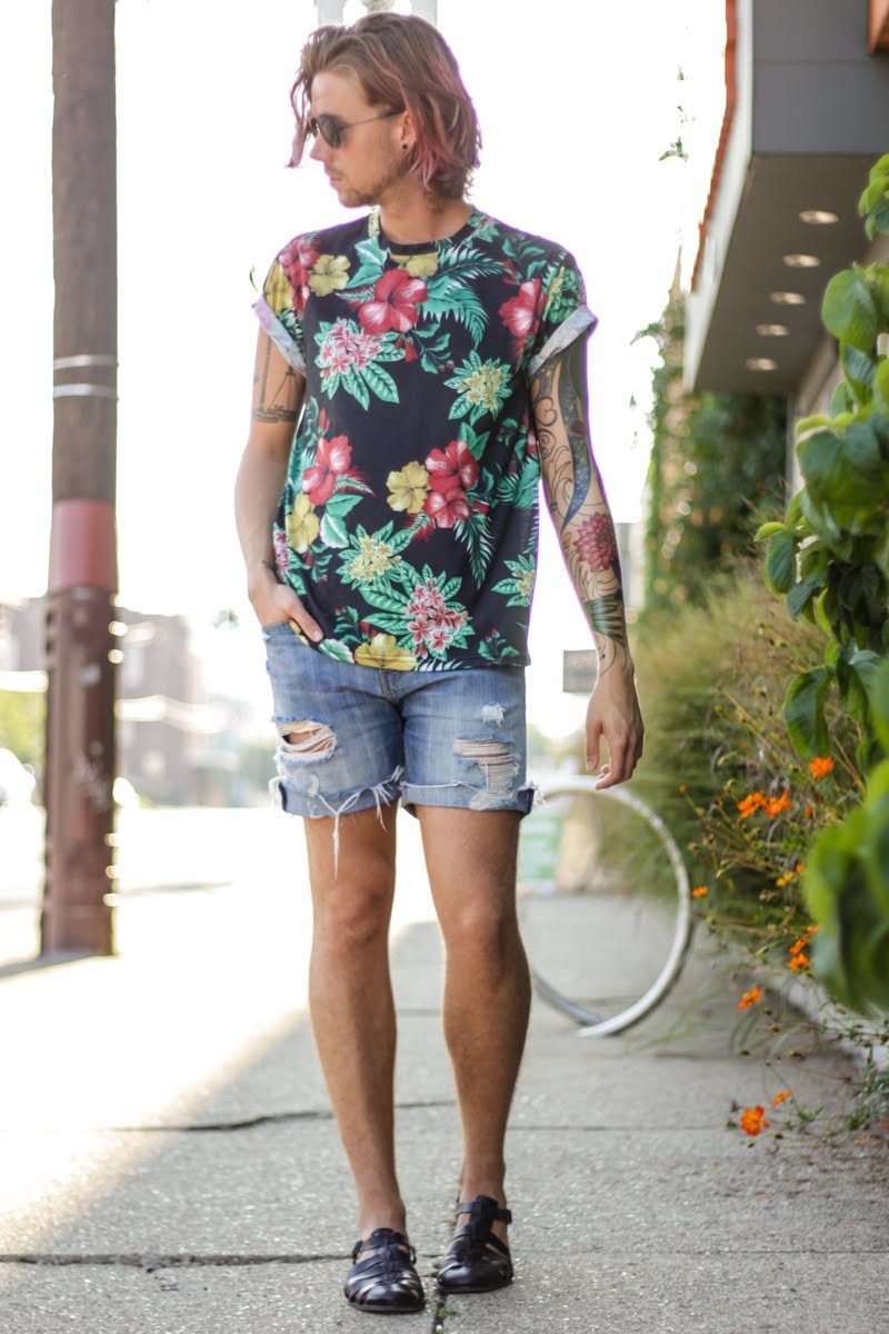 Man wearing floral print t-shirt and distressed denim shorts on a sunny sidewalk