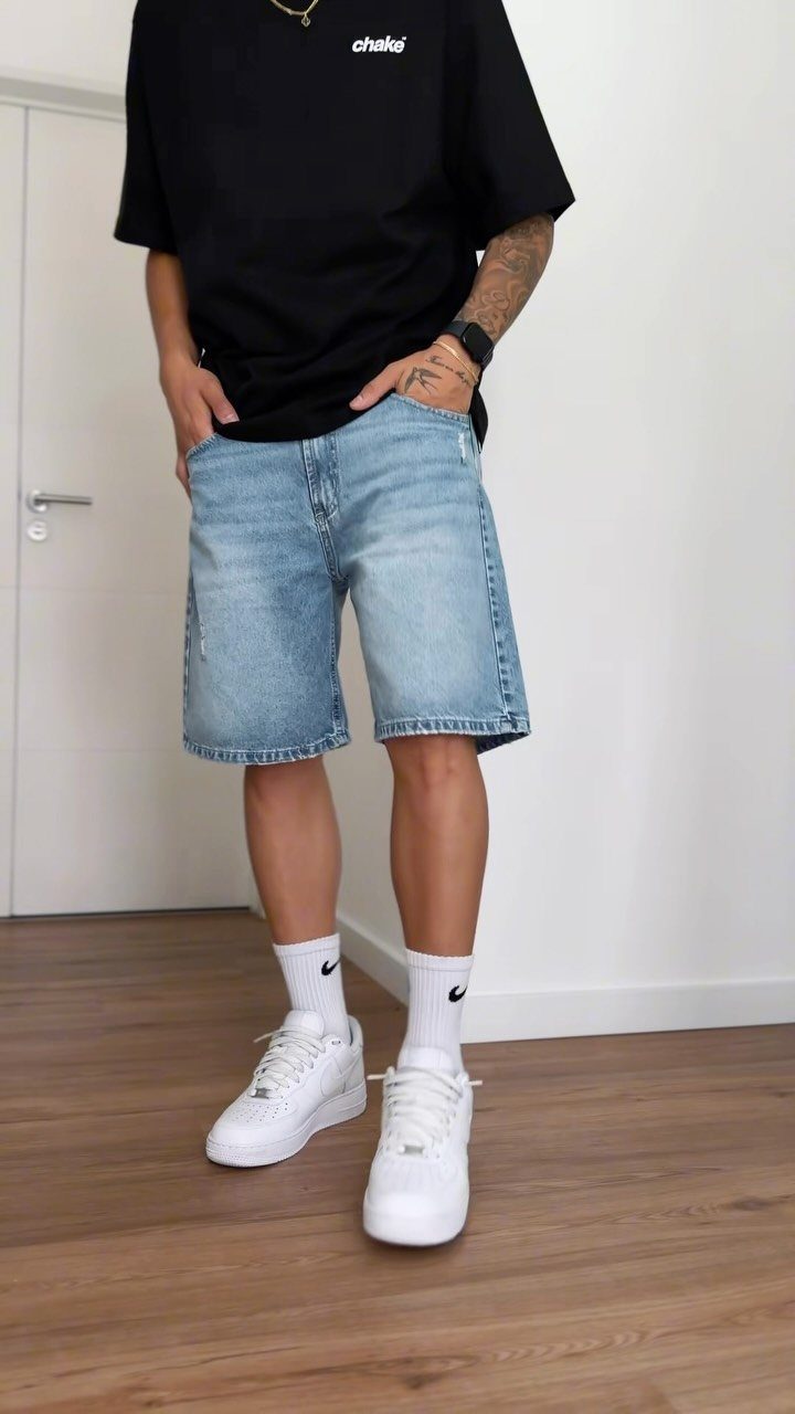 Person wearing a black graphic t-shirt, light blue denim shorts, and white sneakers.