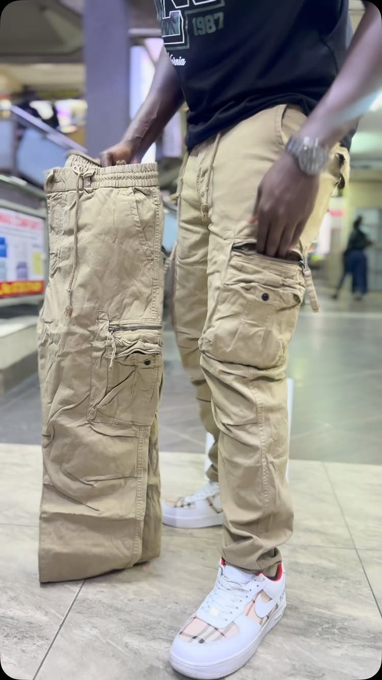 Person wearing khaki cargo pants and white sneakers holding another pair of pants.