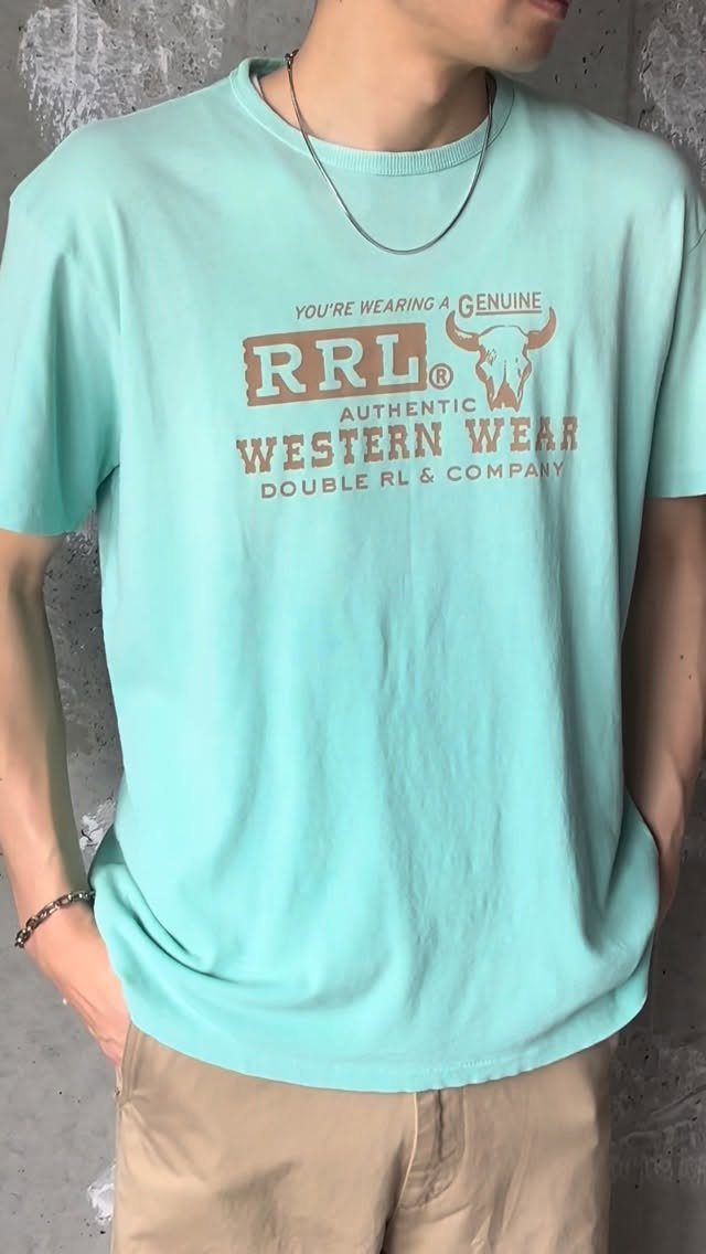 Person wearing a turquoise graphic t-shirt and khaki pants against a grey wall.