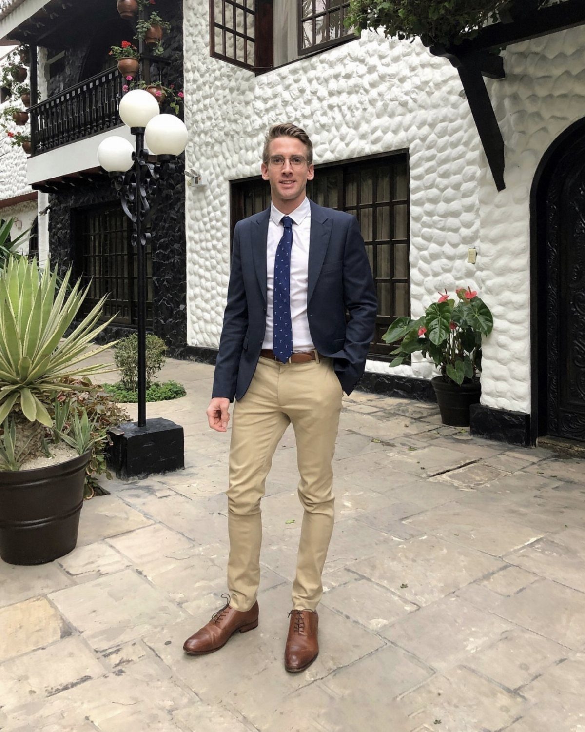 Man wearing a navy blue blazer and khaki pants standing in a courtyard