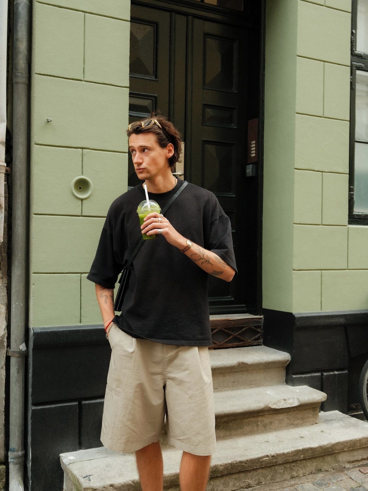 Man wearing a black oversized t-shirt and wide khaki shorts standing outdoors.