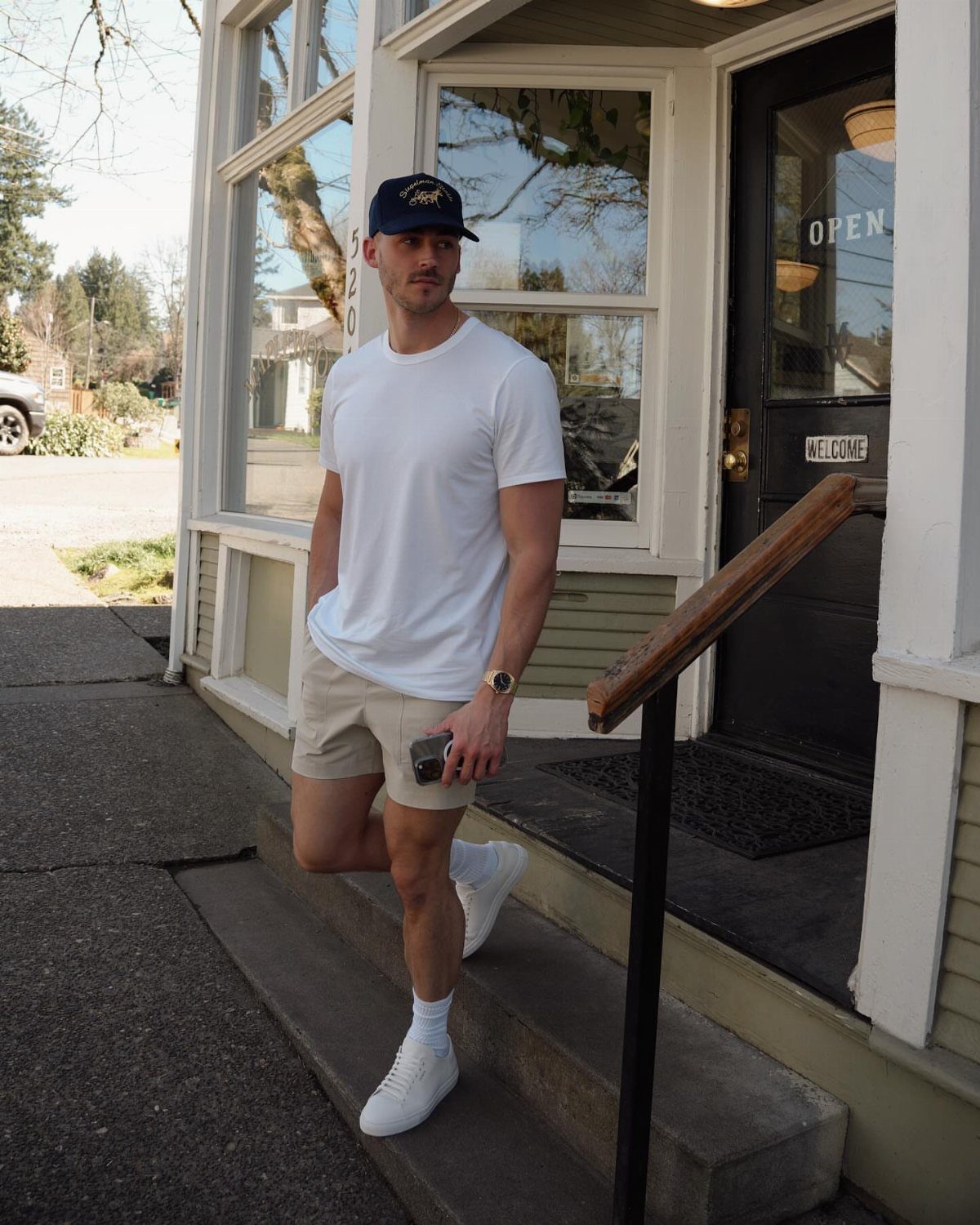 Man wearing a white t-shirt, khaki shorts, and white sneakers standing outdoors.