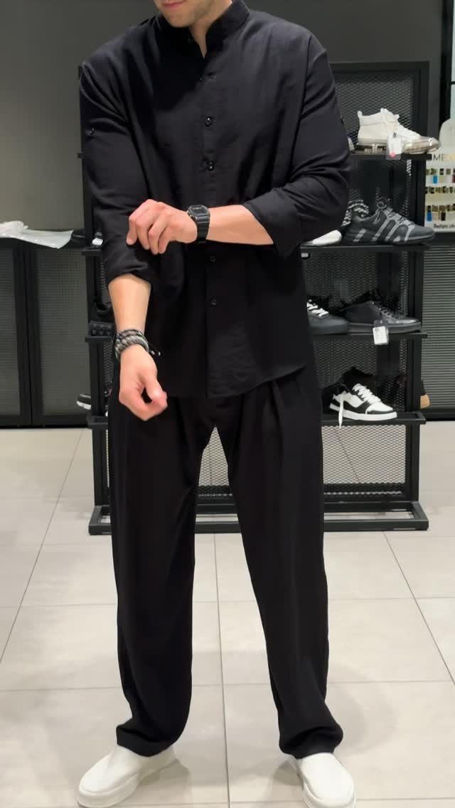 Man wearing a black button-down shirt and black wide-leg linen pants with white sneakers