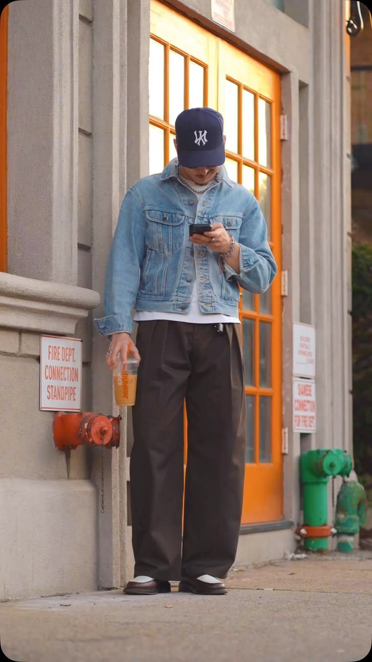 Man wearing a denim jacket, white tee, and wide-leg brown linen pants outdoors.