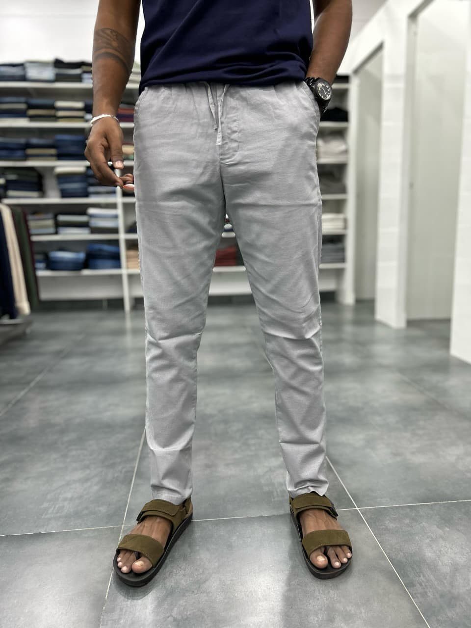 Man wearing light grey drawstring linen pants, a navy t-shirt, and olive sandals.