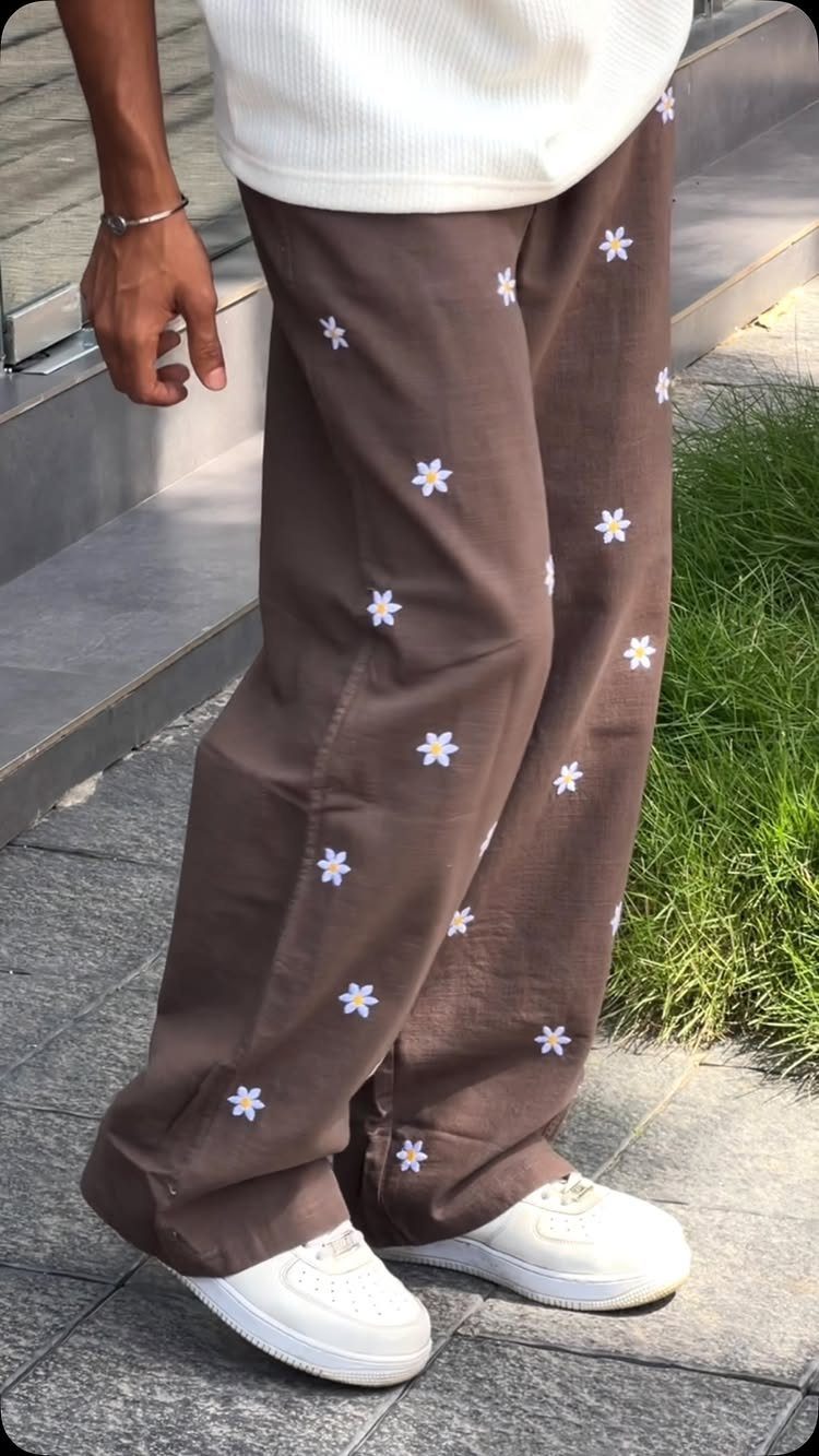 Man wearing brown linen pants with white flower embroidery and white sneakers.