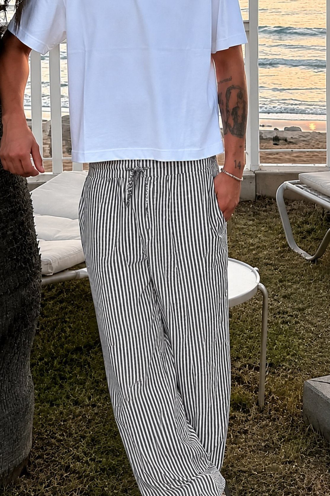 Man wearing a white t-shirt and blue and white striped linen pants outdoors.