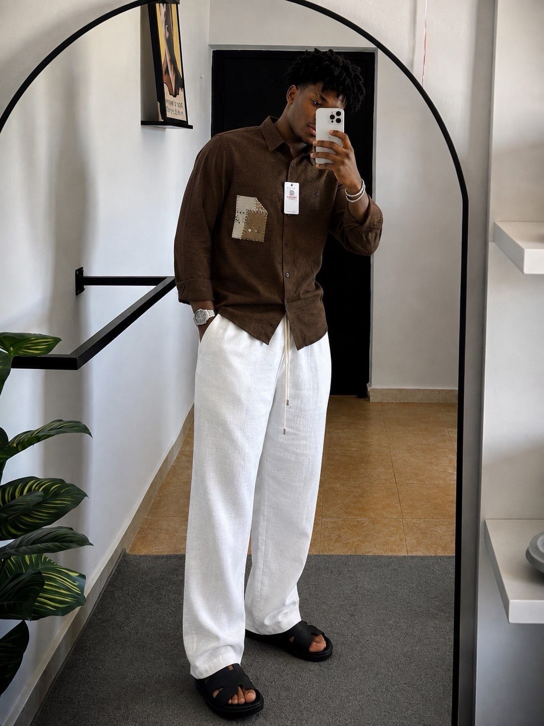 Man wearing a brown linen shirt and white wide-leg linen trousers with black slides.