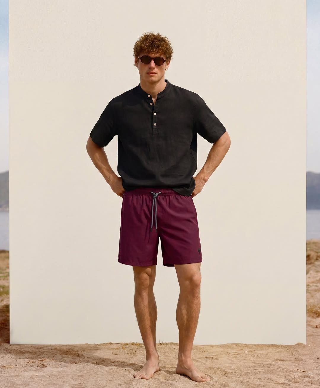 Man wearing a black linen shirt and purple swim shorts on a beach