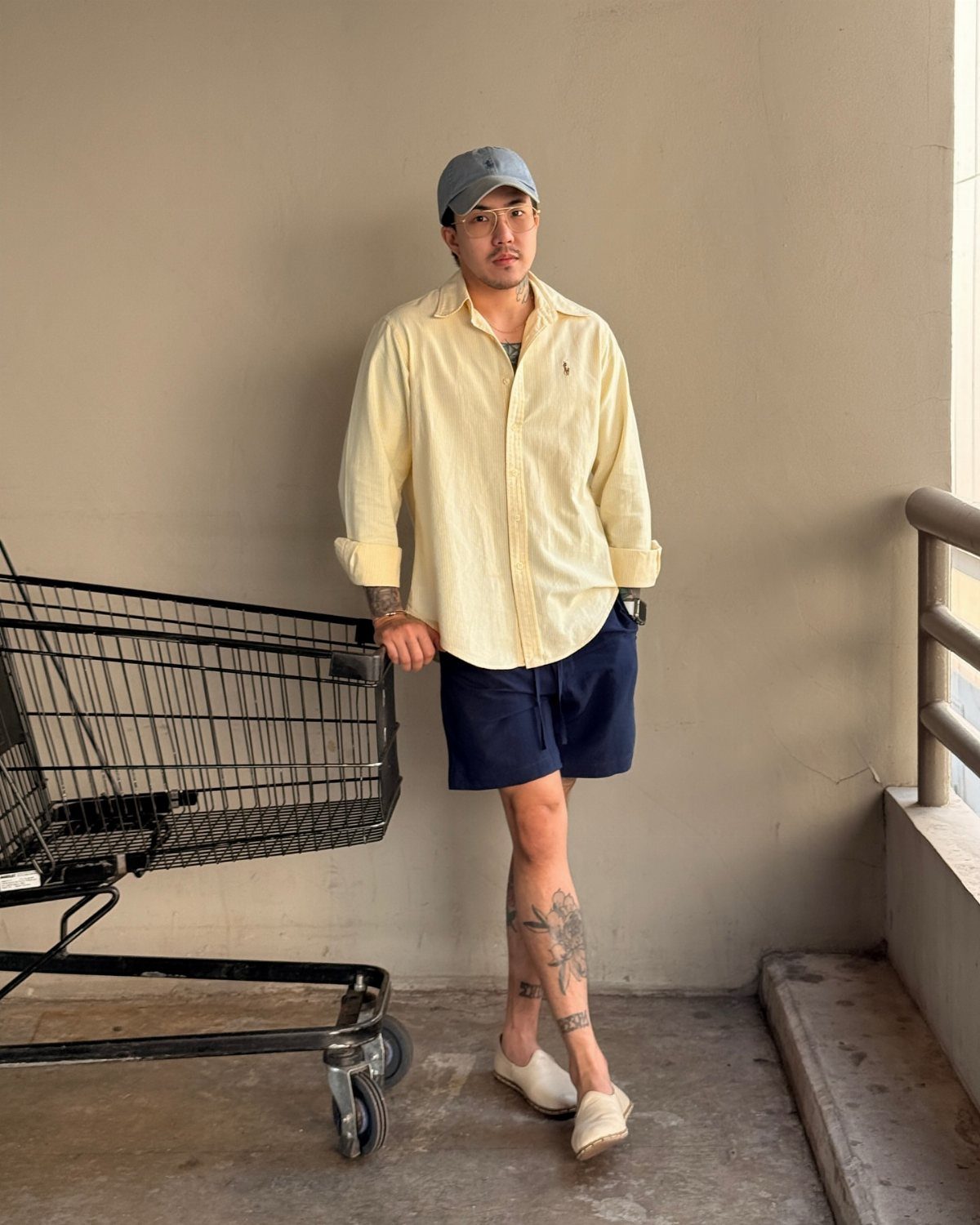 Man wearing an untucked yellow linen shirt with navy shorts and white shoes.