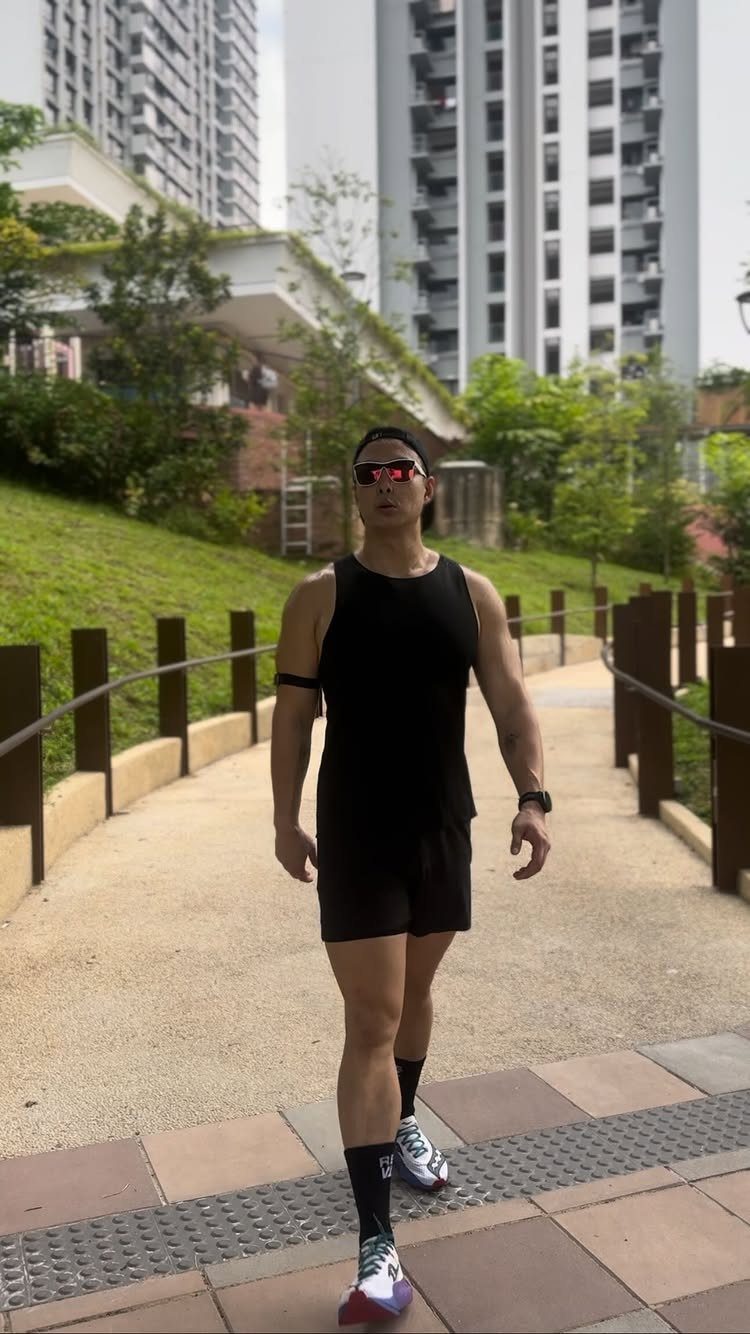 Muscular man in black athletic tank top and shorts walking on outdoor path