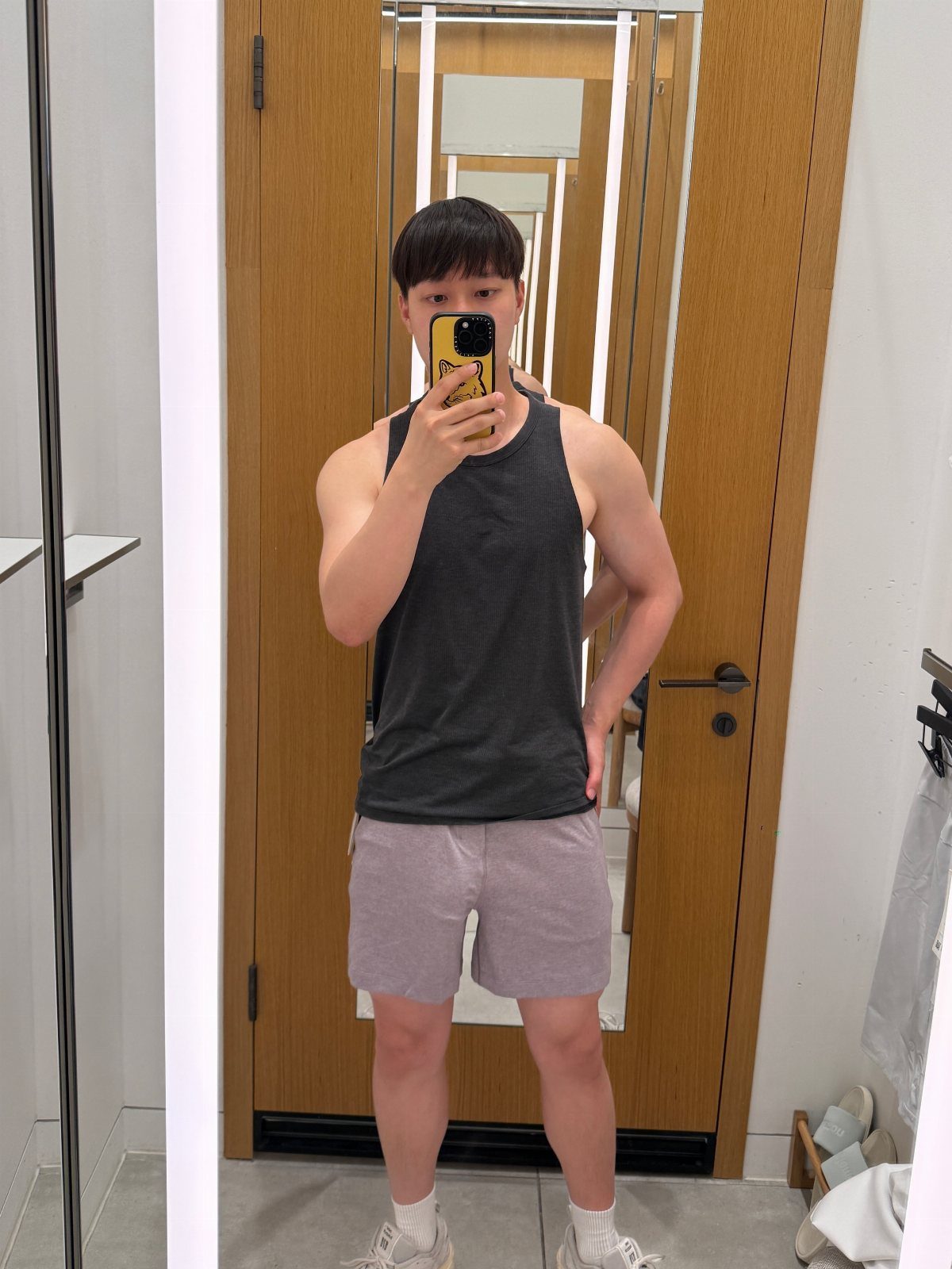 Man in a grey tank top and purple shorts taking a mirror selfie.