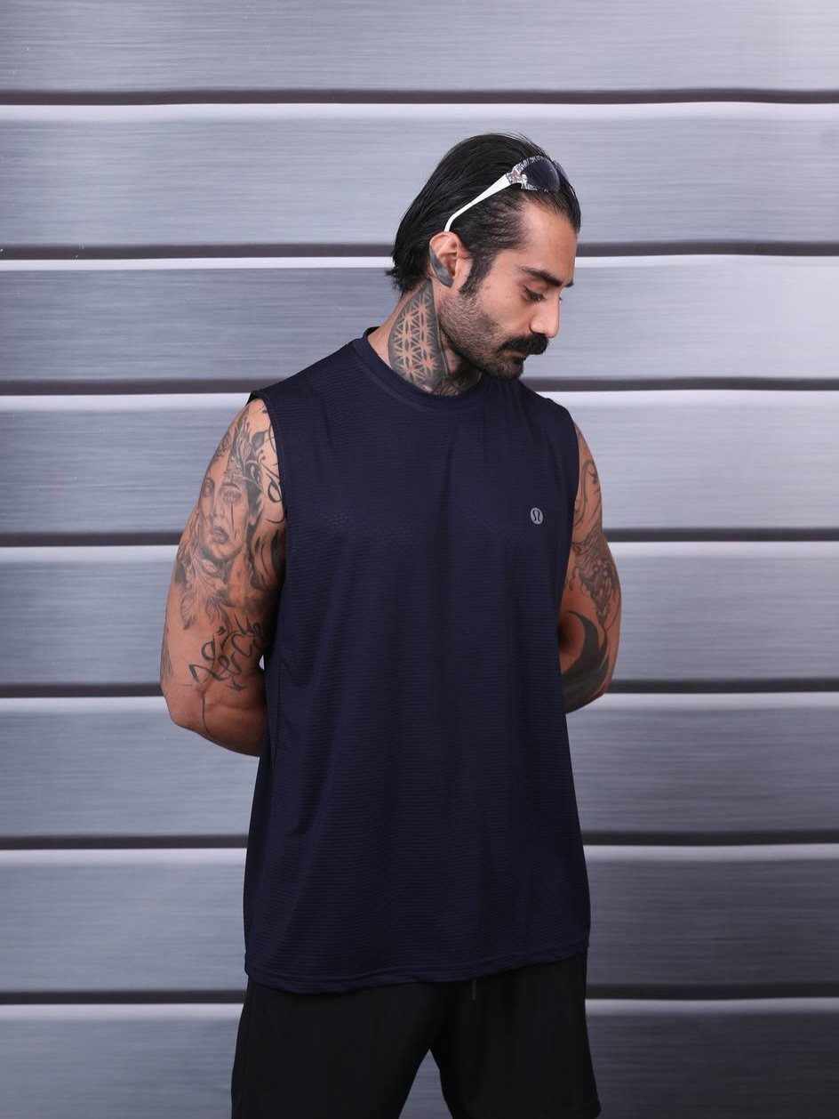 Man with tattoos wearing a navy blue sleeveless gym shirt and black shorts.
