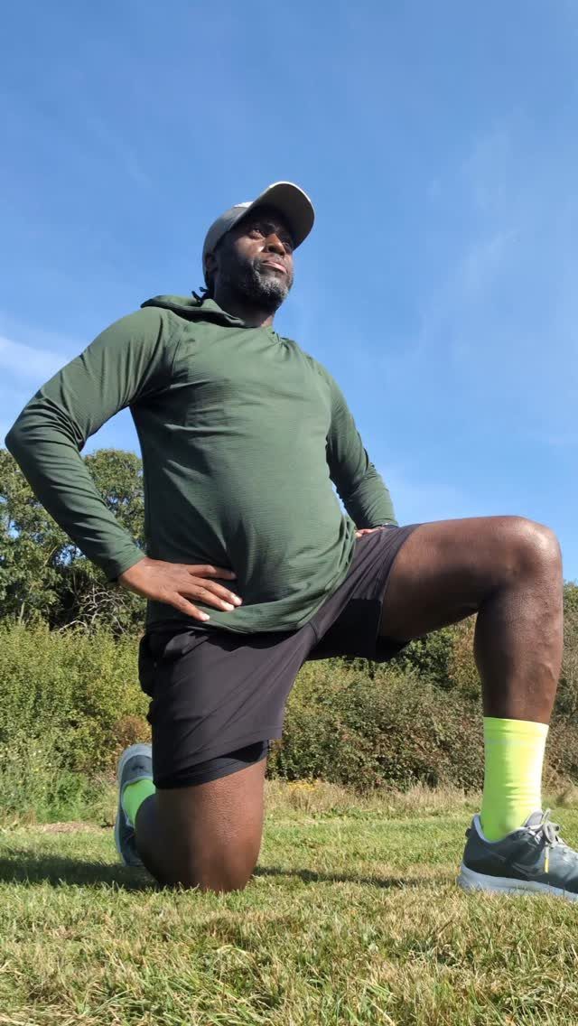 Man in olive green athletic wear and black shorts lunging on grass.
