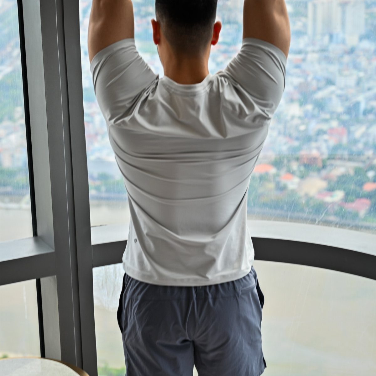 Man in white t-shirt and grey shorts stretching by a city window