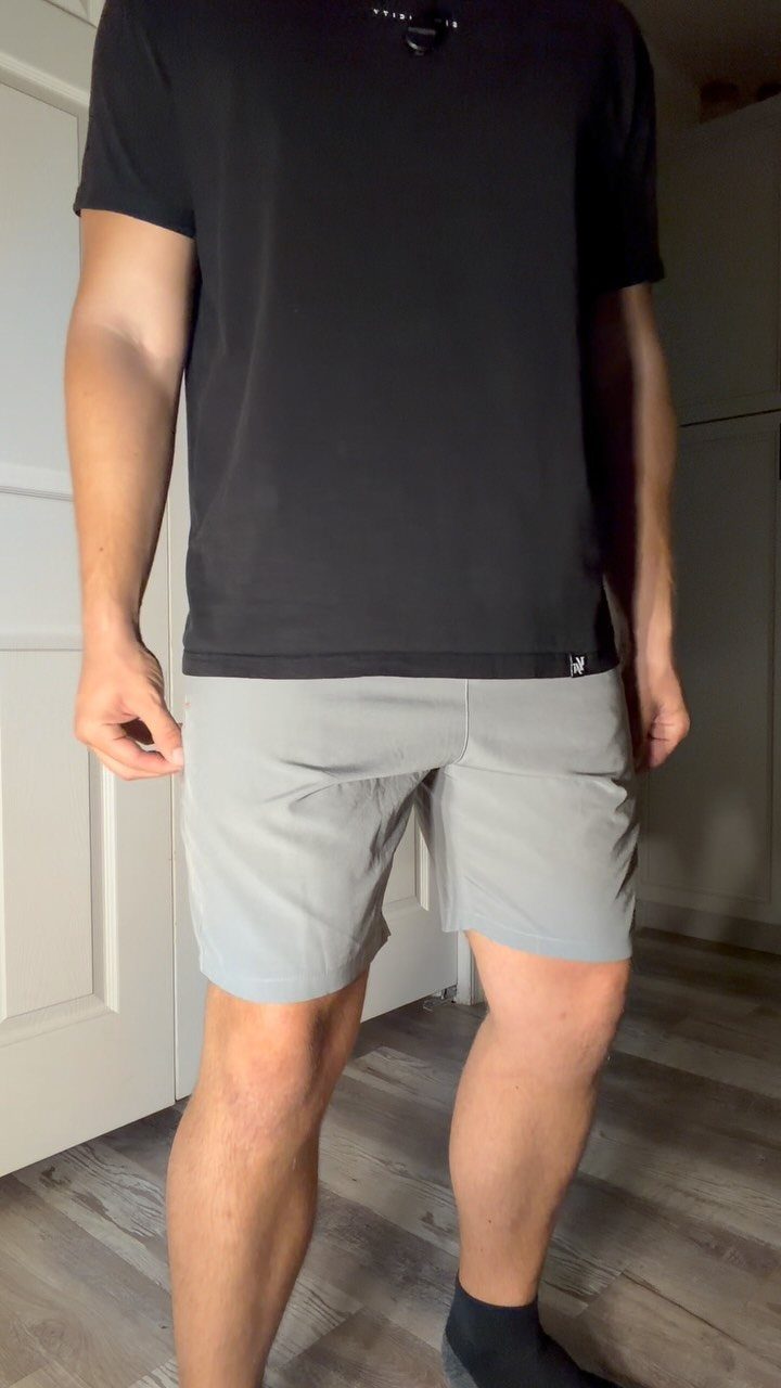 Person wearing a black t-shirt and light grey athletic shorts standing indoors.