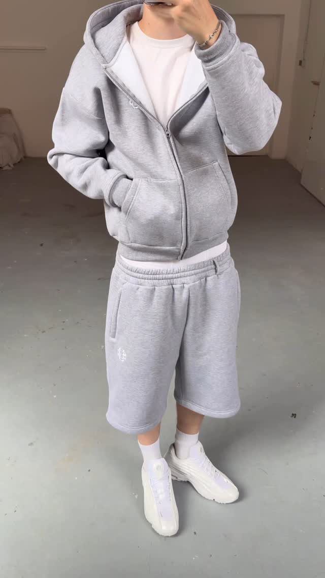 Person wearing a grey hoodie and matching grey shorts with white sneakers.