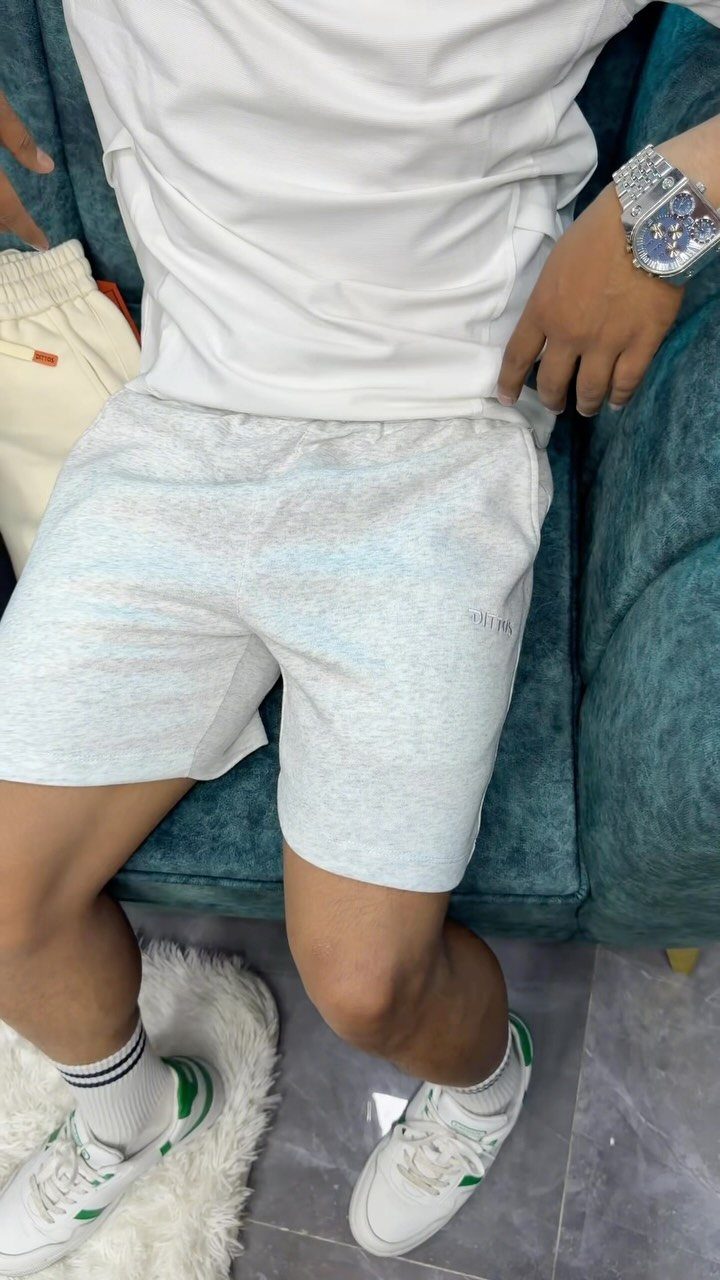 Person wearing white t-shirt, grey shorts, and white sneakers sitting on teal sofa.