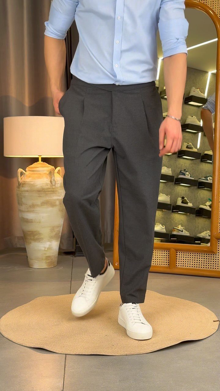 Man wearing dark grey pleated trousers, light blue shirt, and white sneakers.
