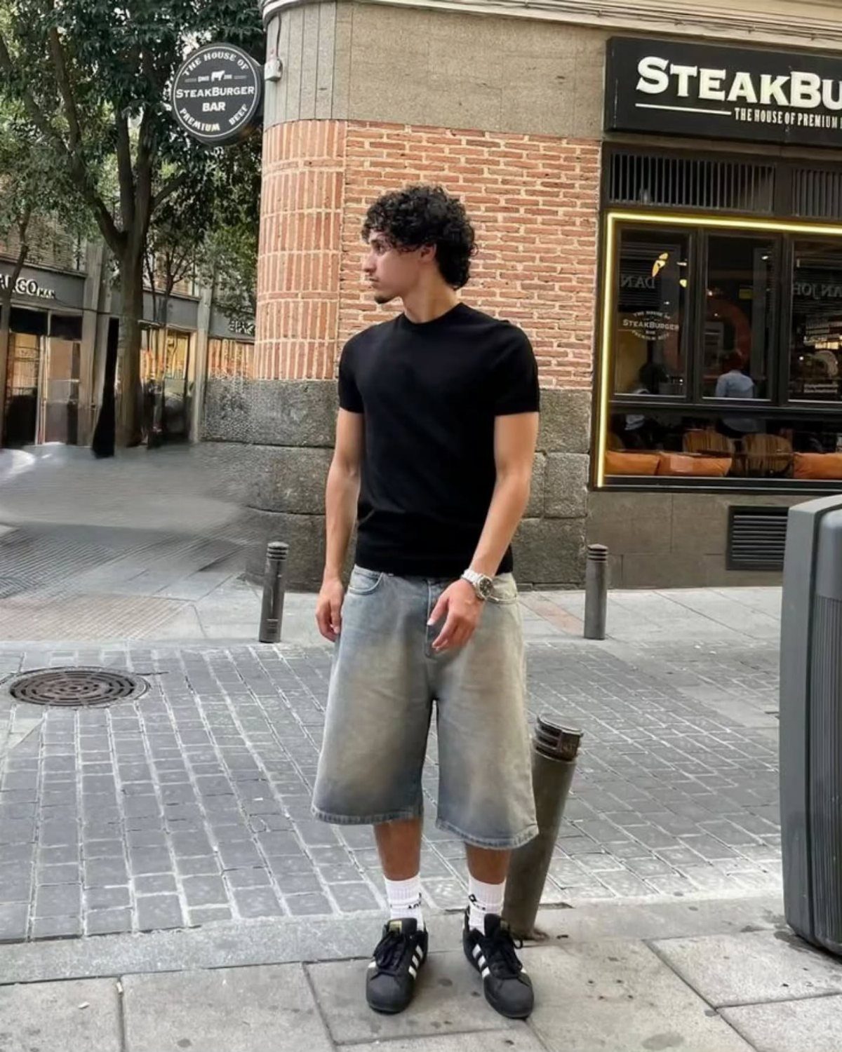 Man wearing a black t-shirt and light blue denim shorts on a city street