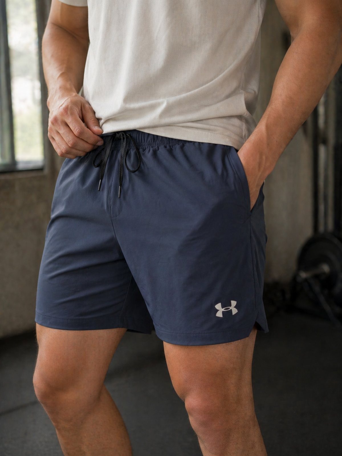 Man wearing navy blue athletic shorts and a white t-shirt in a gym.
